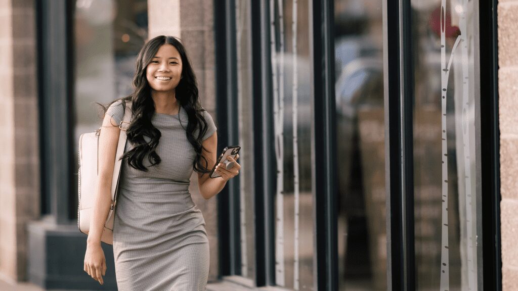 Smiling woman holding phone while walking outside.