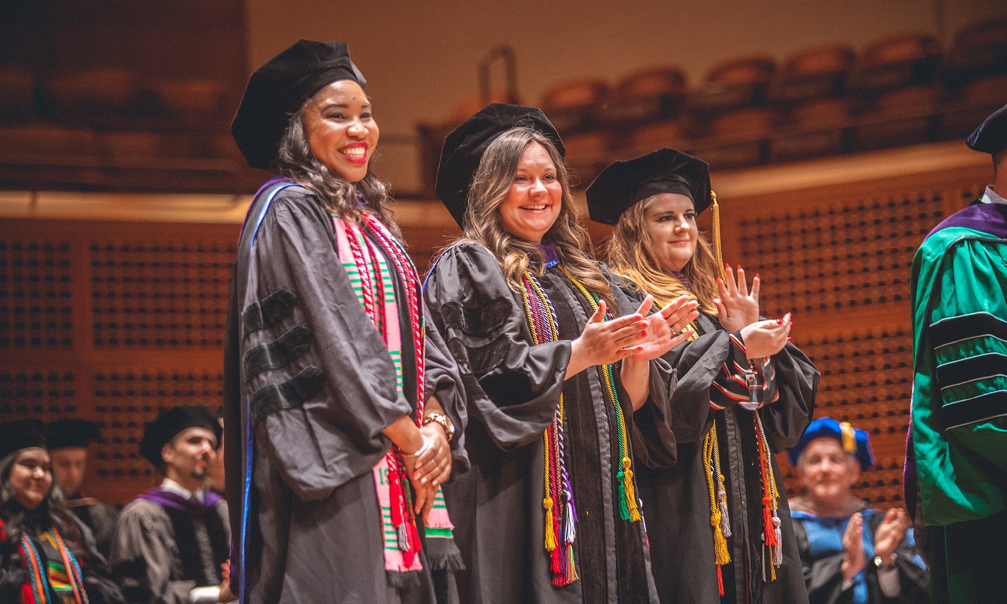 Happy graduates clapping at graduation.